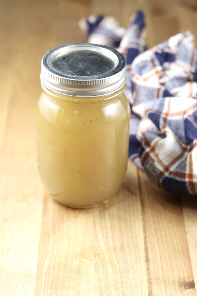 Homemade chicken broth in a mason jar, plaid towel to the side on butcher block counter