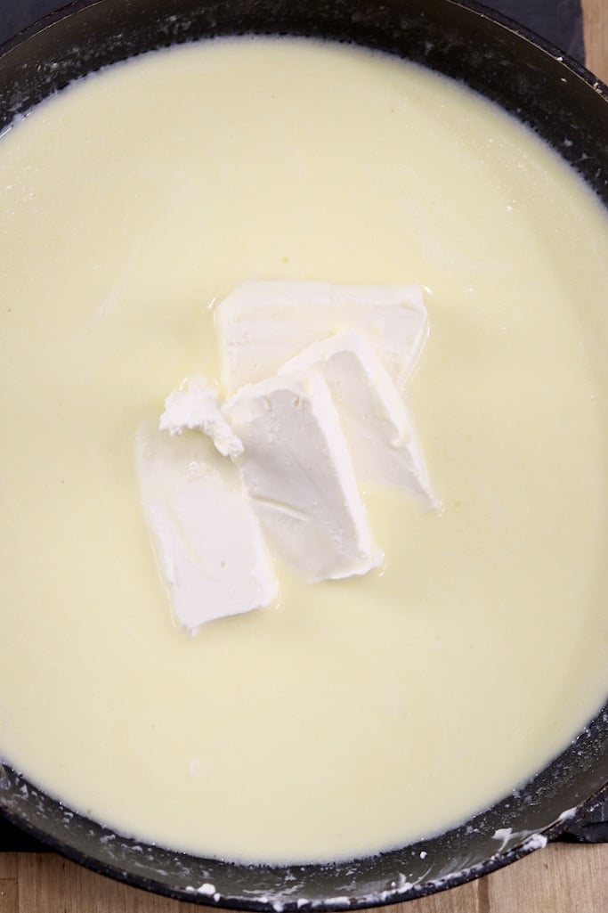  Adding chunks of cream cheese to Alfredo sauce in a skillet