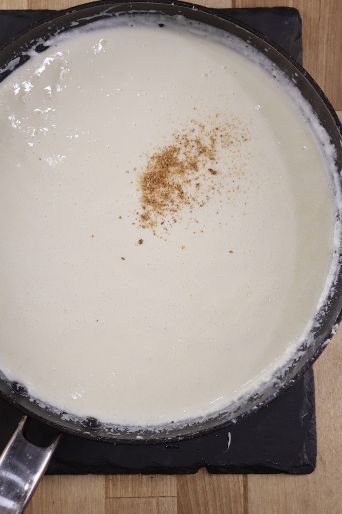 Adding nutmeg to Alfredo sauce in a skillet