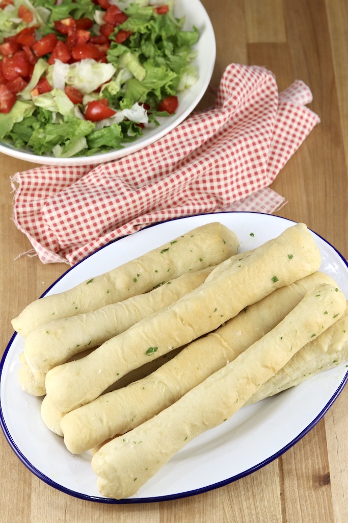 Breadsticks on a platter, red napkin, salad with tomatoes