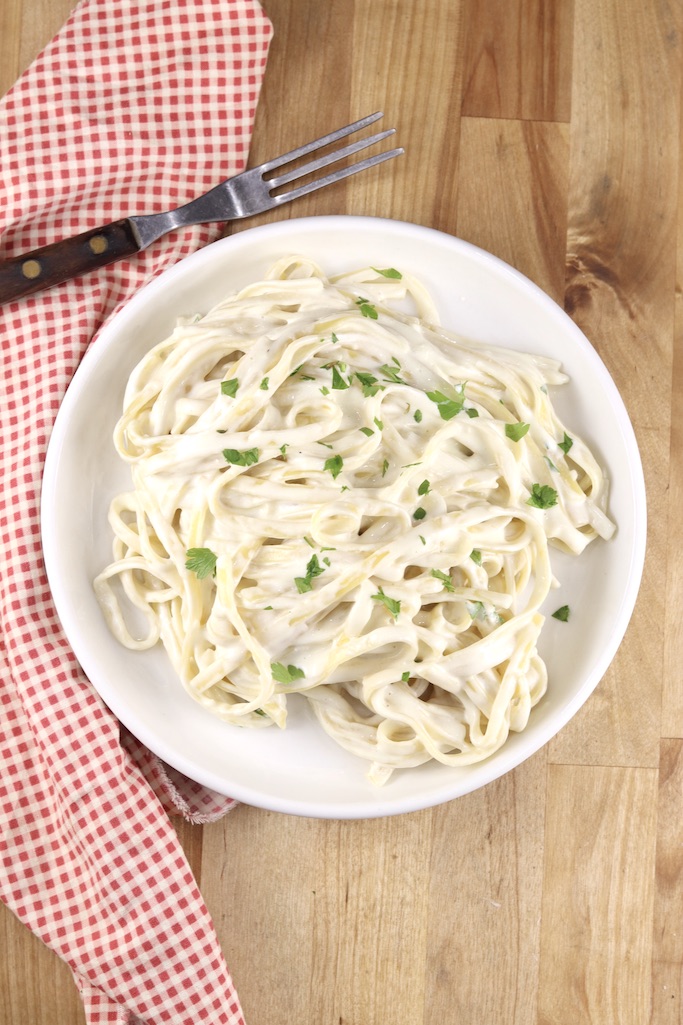 Creamy fettuccine Alfredo on a white plate, red napkin and fork on a wood table