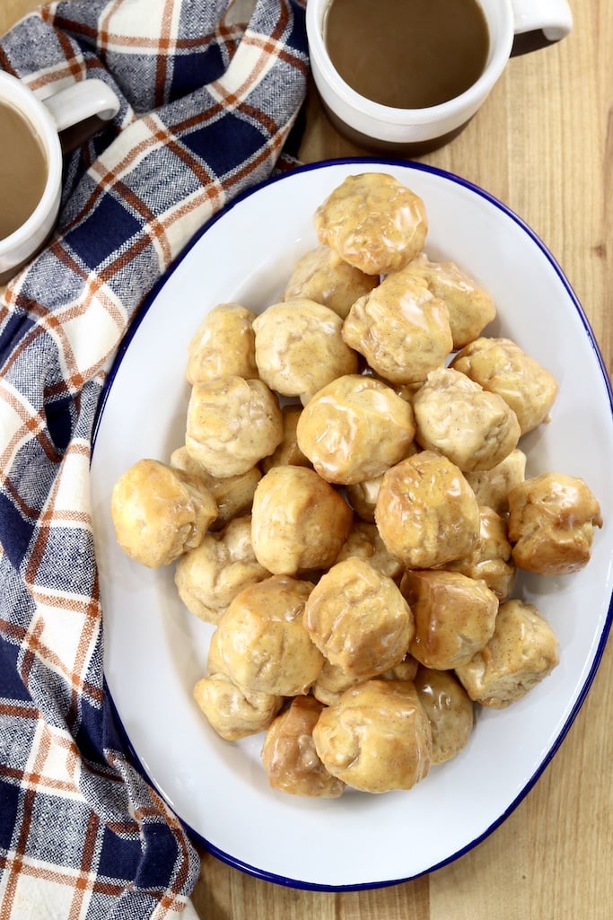 Maple Donut Holes on an oval platter with plaid napkin and 2 cups of coffee, overhead view