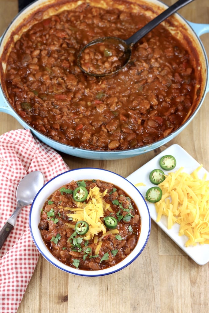 Smoked Pork Chili served in a bowl, dutch oven with chili, garnish plate with cheese and jalapenos