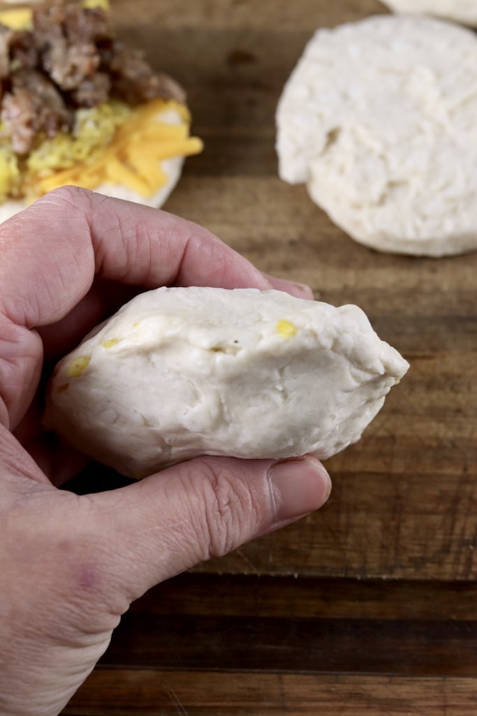 Pinching biscuits together around filling for pocket breakfast sandwiches