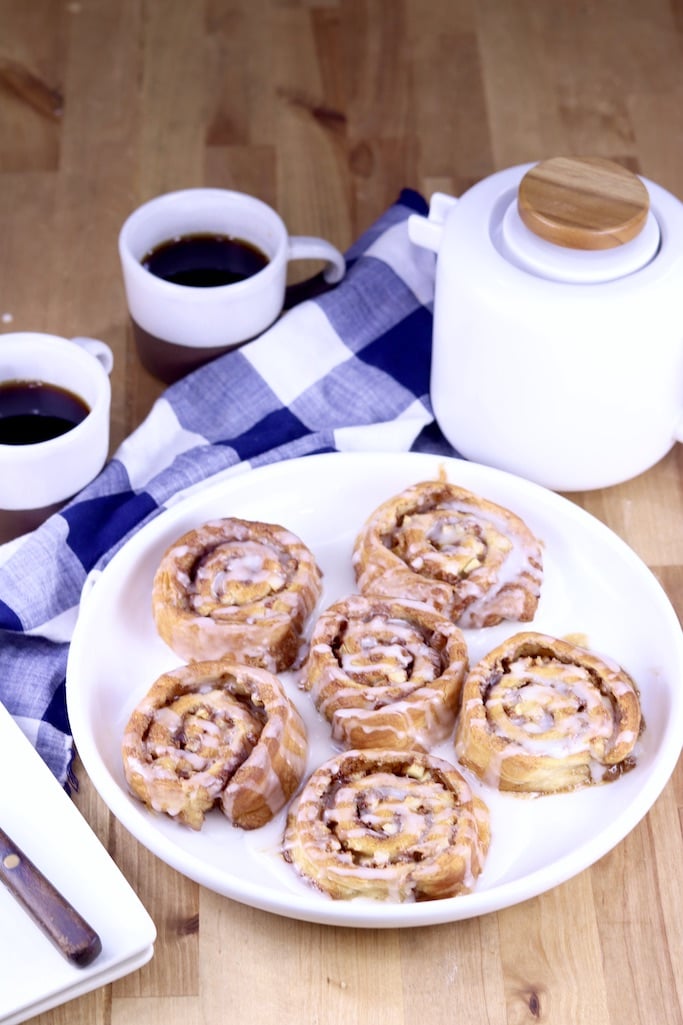 Apple Cinnamon Rolls on a white plate, white coffee pot and 2 cups of coffee with a blue napkin