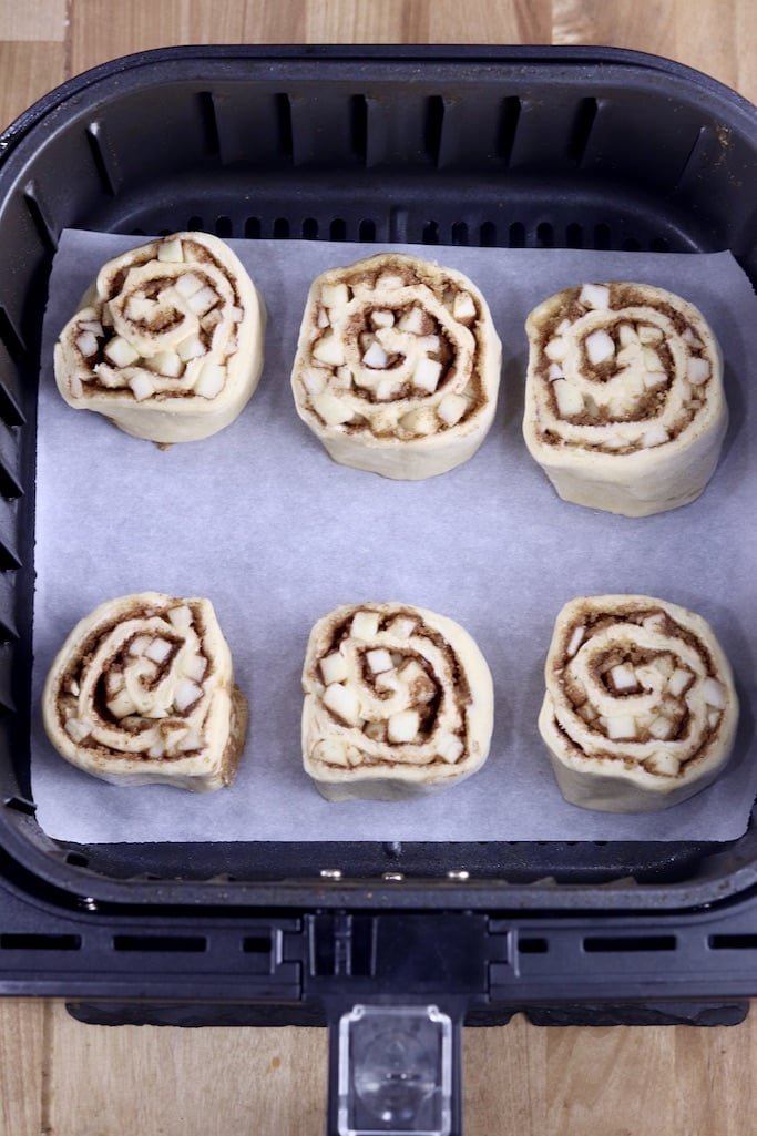 Air fryer basket lined with parchment, 6 uncooked cinnamon rolls