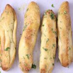4 garlic butter breadsticks with parsley on parchment paper