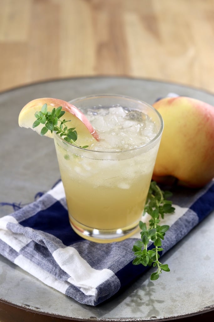Apple Cider Cocktail with an apple and thyme garnish, on a tray with an apple and blue towel