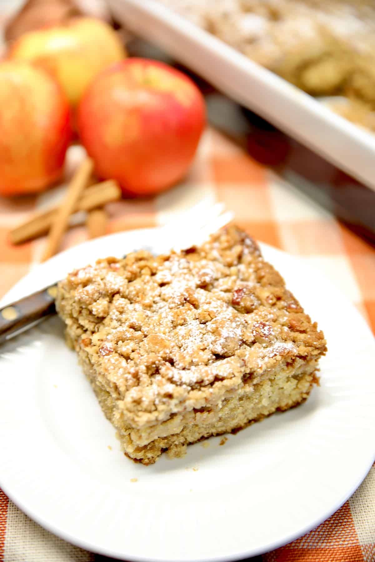Apple coffee cake on a plate, apples in background.