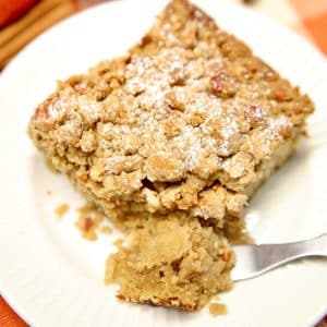 Slice of apple coffee cake on a plate with bite on fork.