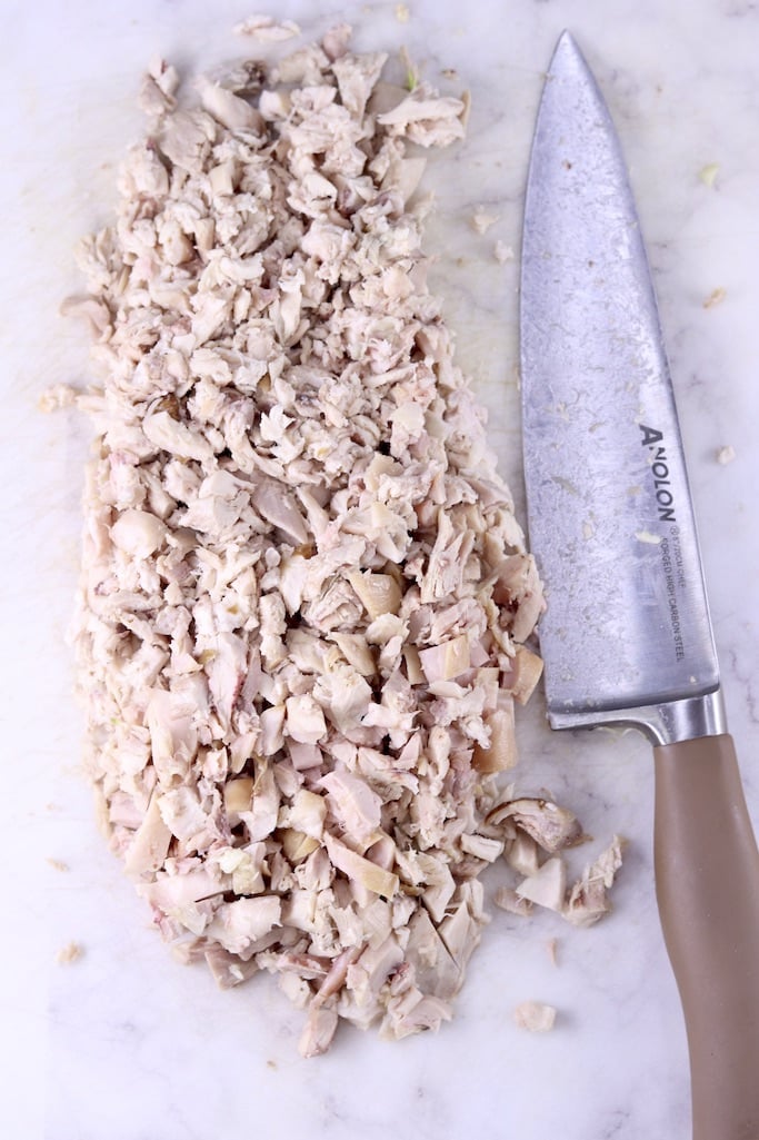 Diced cooked chicken on a white board with a chef knife