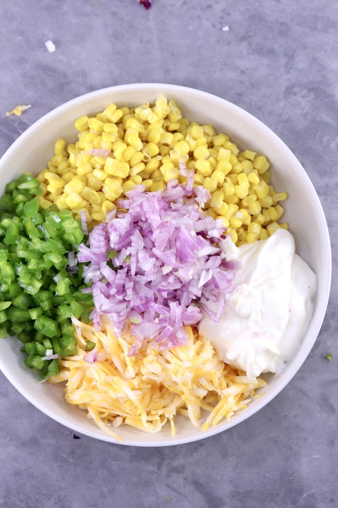 Bowl with corn, red onion, bell pepper, shredded cheese, not mixed