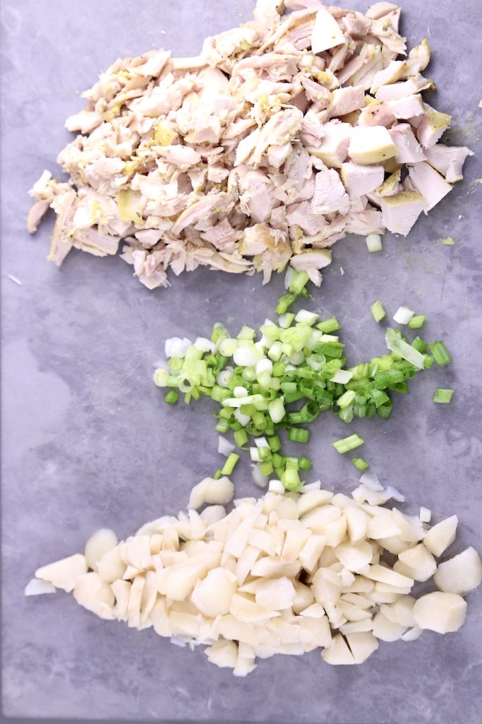 Diced chicken, diced green onions, water chestnuts on a gray cutting board