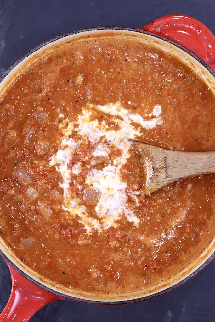 Adding cream to tomato sauce in a pan with wooden spoon