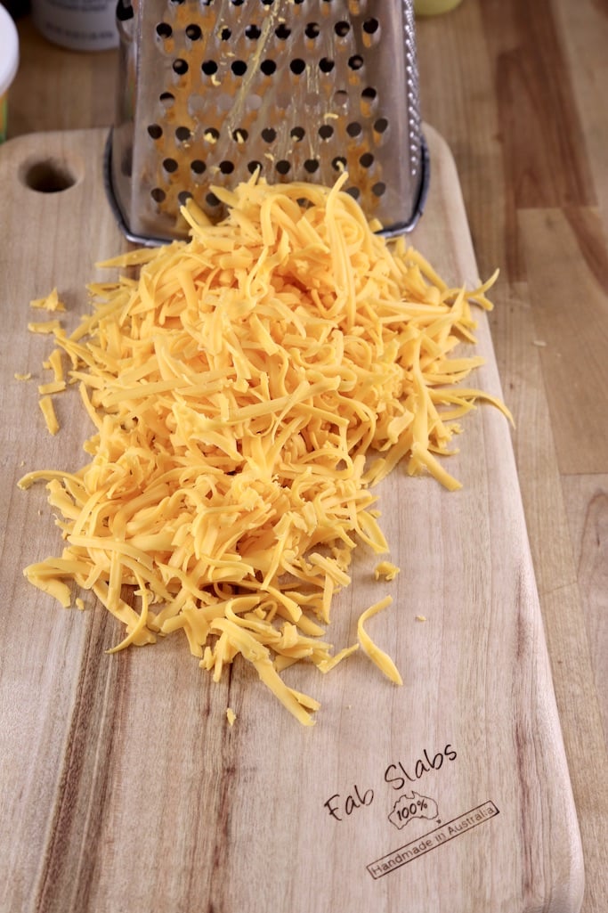 Shredded colby cheese on a wood cutting board with grater