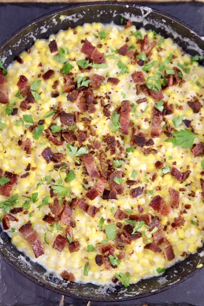 Overhead view of cream corn topped with bacon and parsley