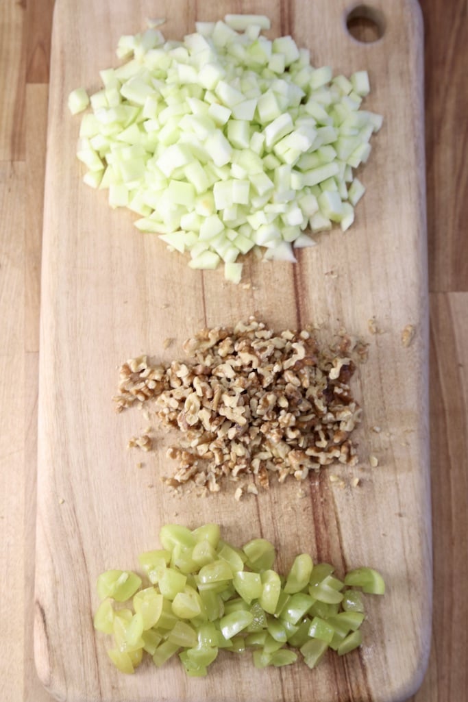 cutting board with diced apples, chopped walnuts and chopped grapes