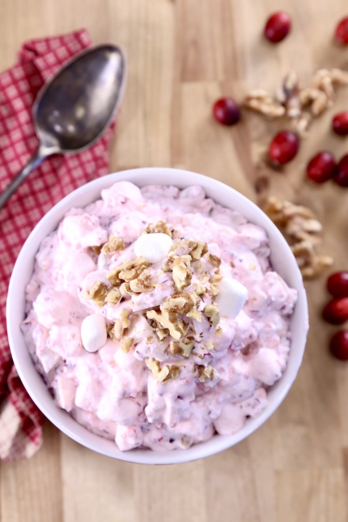 Cranberry Fluff Salad topped with walnuts - fresh cranberries and walnuts to one side, serving spoon on the other