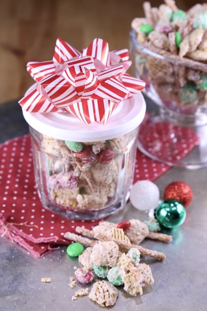 Small jar of white trash snack mix with a red and white bow. Snack mix scattered in front