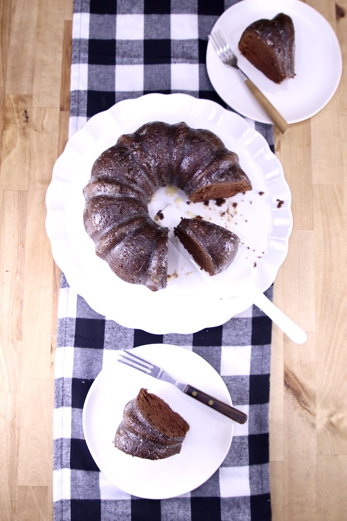 Overhead view of chocolate bundt cake sliced, 2 dessert plates with slices over a black plaid table runner
