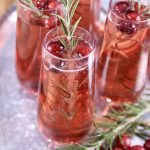 Cranberry mimosa cocktails on a tray with rosemary and cranberry garnish