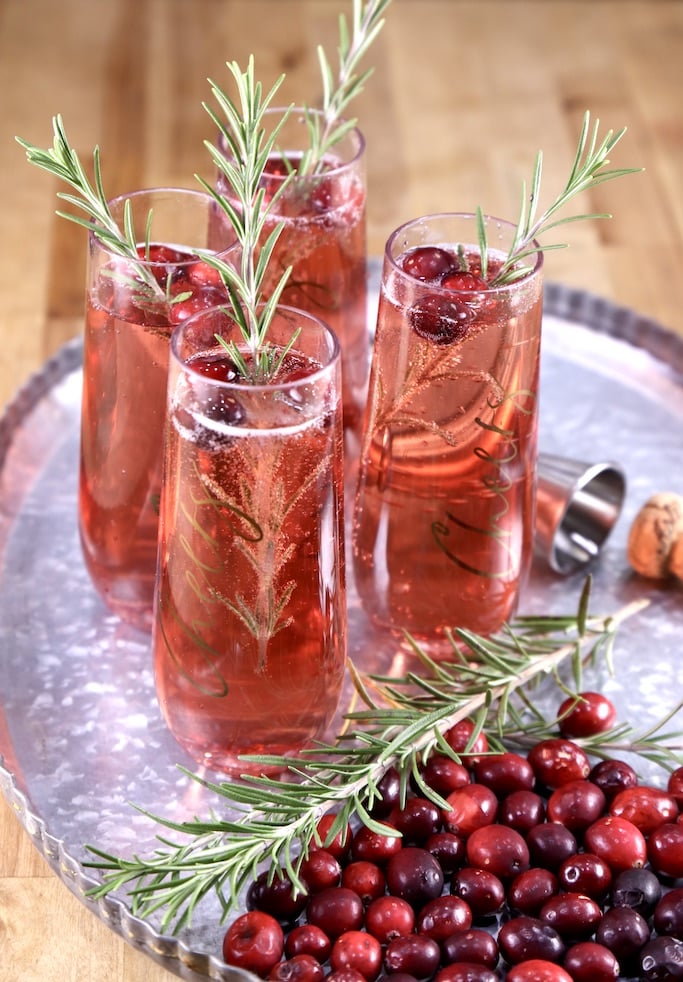 4 cranberry mimosa cocktails on a tray with fresh rosemary and cranberries