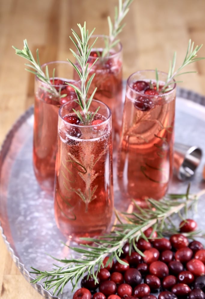Tray with 4 cranberry mimosa cocktails with rosemary and cranberry garnish