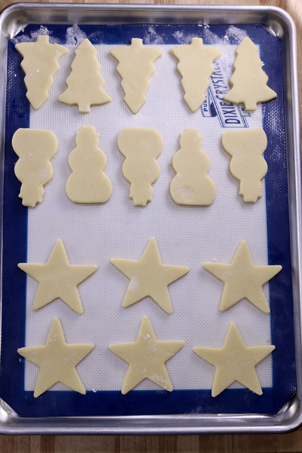 Cookie sheet lined with a silpat. Tree, snowmen and star cut out cookies ready to bake.