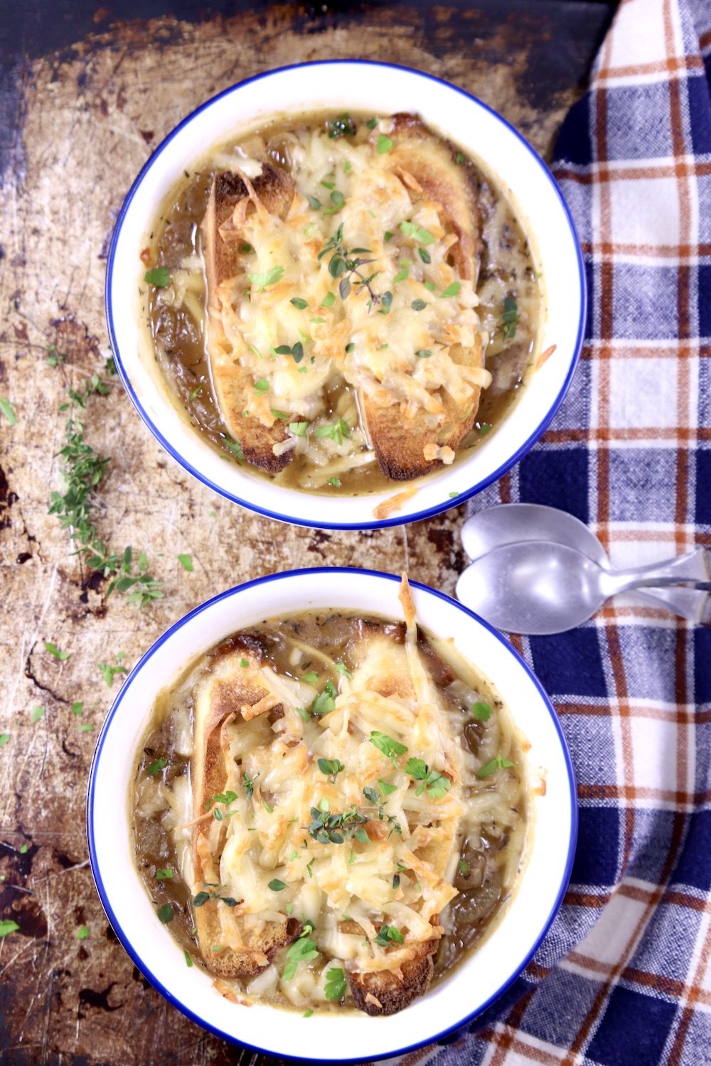Two Bowls of French Onion Soup on a sheet pan with a blue check napkin