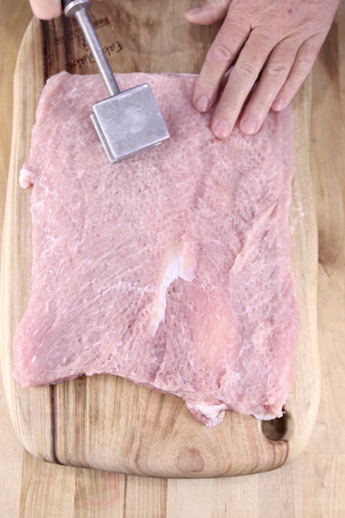 flattening out a sliced open pork tenderloin with a meat mallet