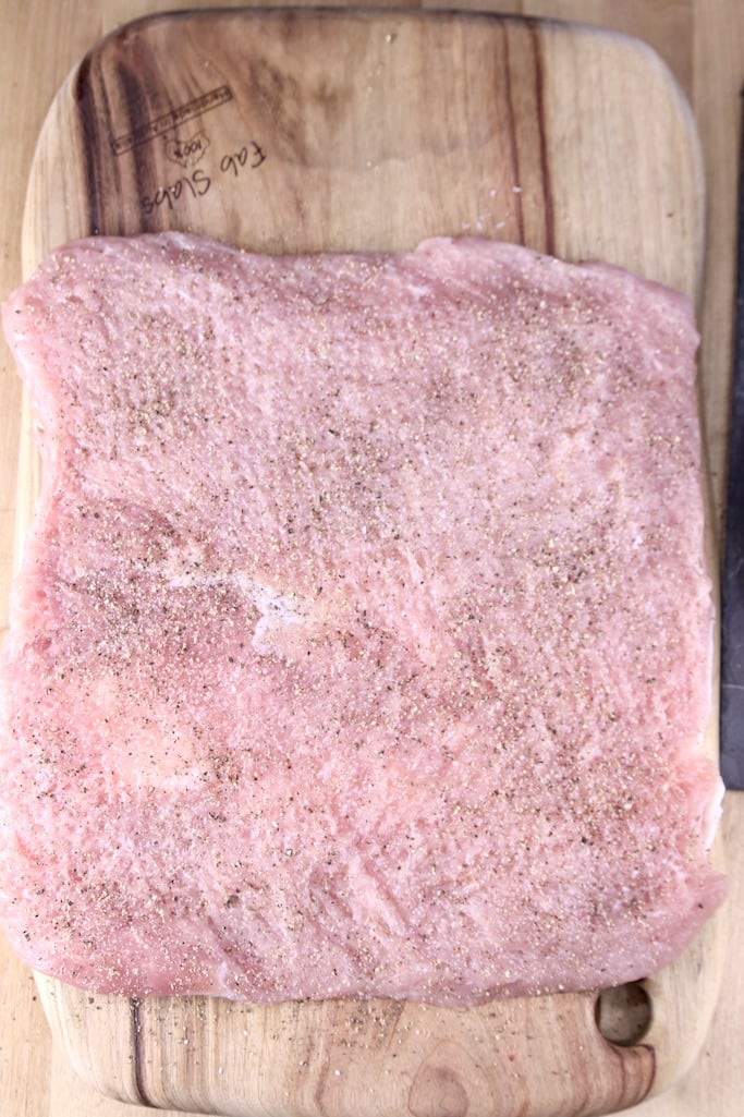 Flattened pork tenderloin with salt and pepper on a cutting board