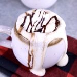 Mudslide Coffee with whipped cream and chocolate drizzle, dripping over the mug onto the red check napkin
