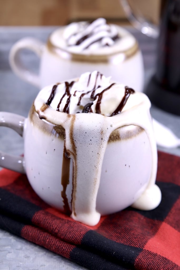Mudslide Coffee topped with whipped cream and chocolate sauce drizzle flowing out of the mug onto a red check napkin