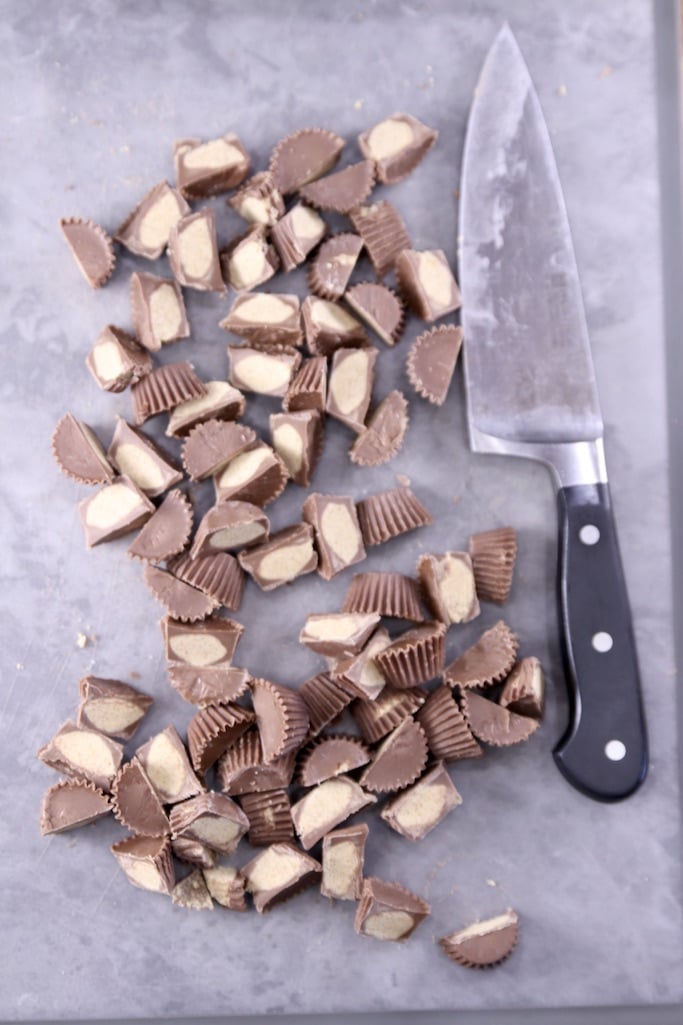 Mini peanut butter cups cut in half on a gray cutting board with a knife