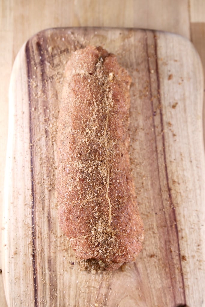 cutting board with pork tenderloin coated in dry rub seasonings