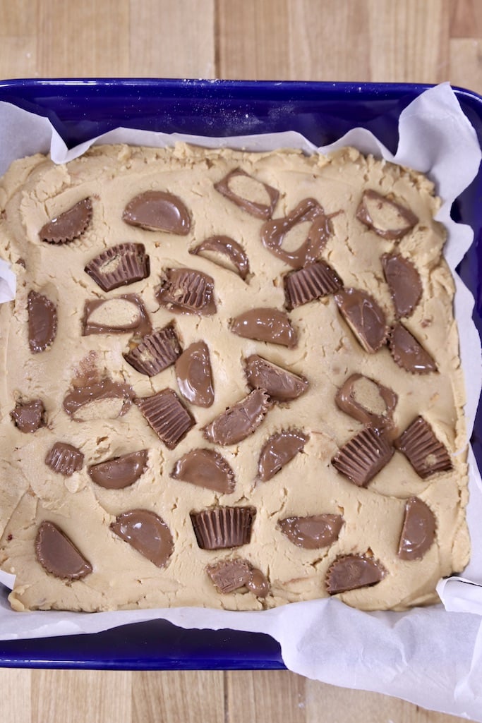 Chopped peanut butter cups pressed into peanut butter fudge in a parchment lined pan