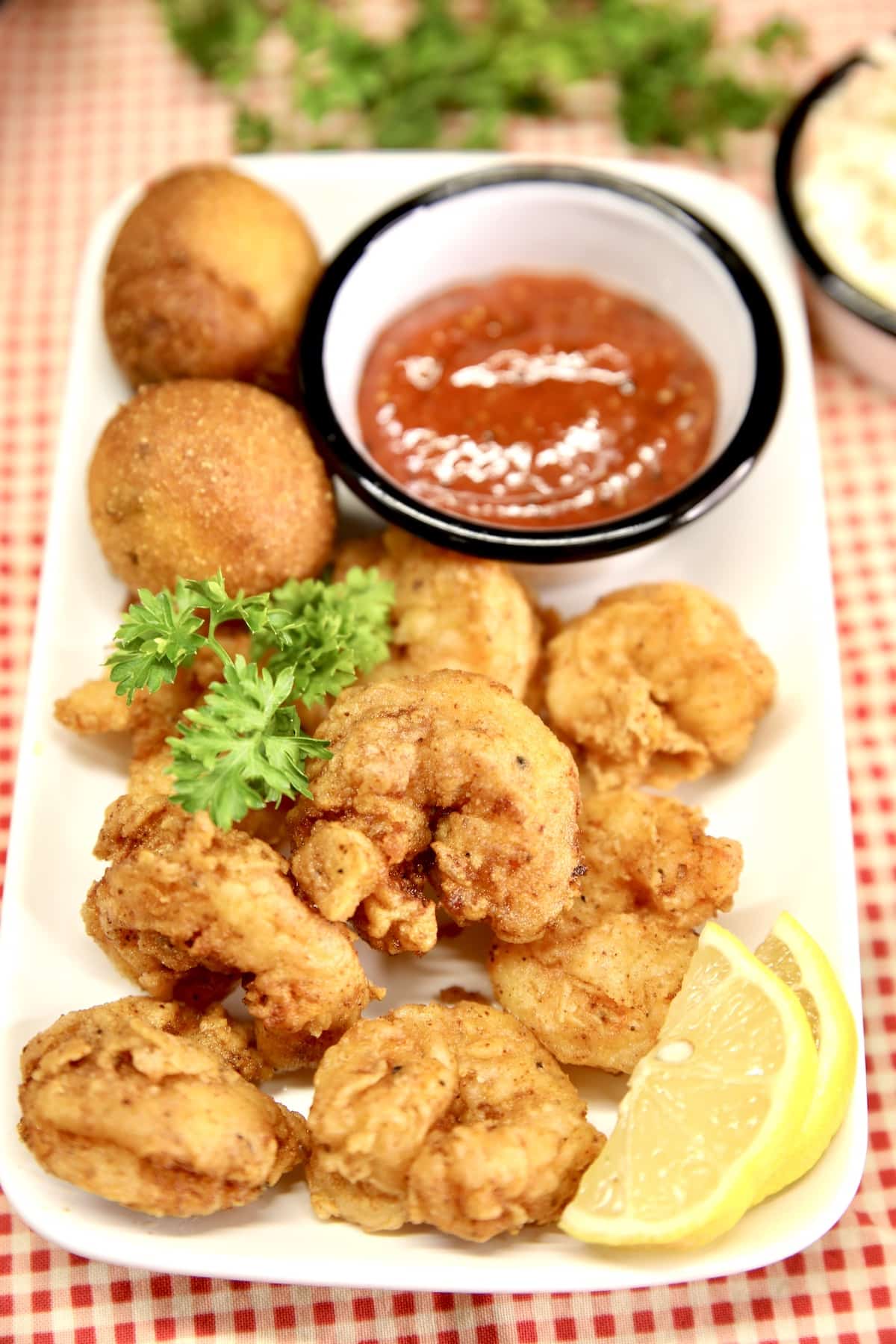 Fried shrimp on a plate with hush puppies, lemon and cocktail sauce.