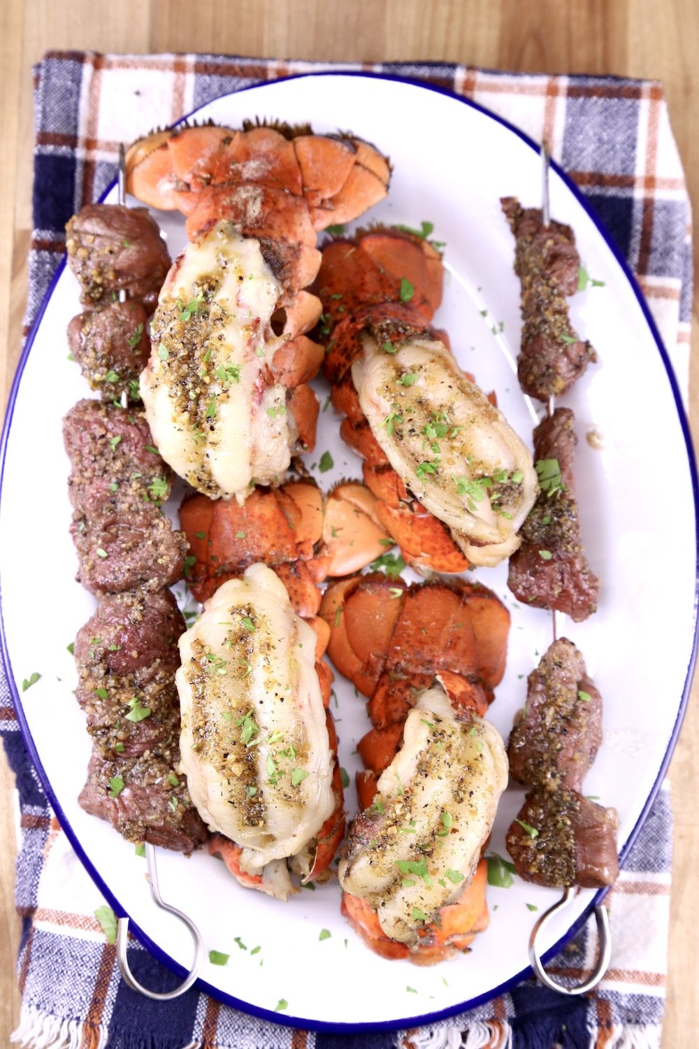 Plaid napkin with oval platter of grilled garlic butter lobster and steak bites