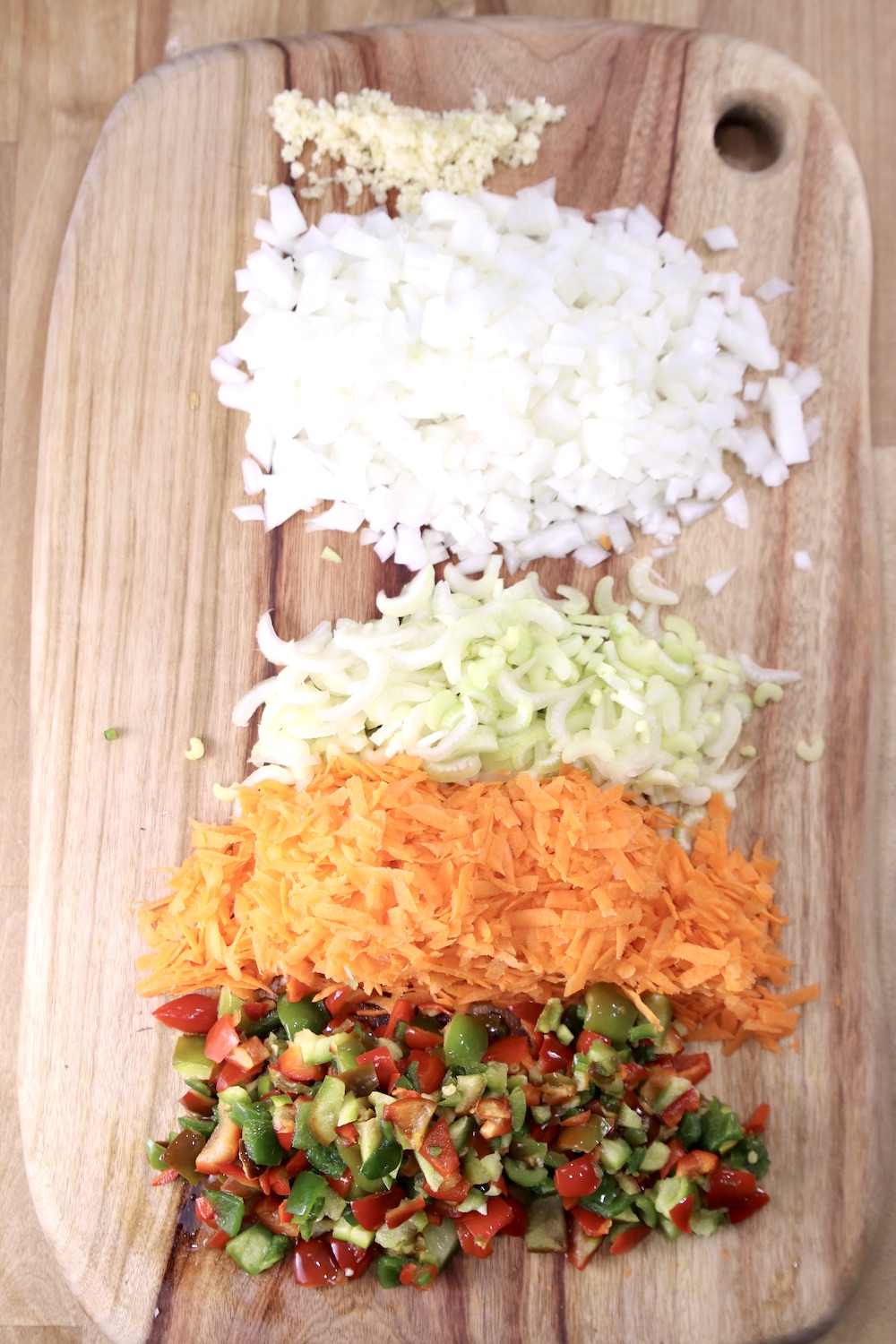 cutting board with garlic, onions, celery, carrots, diced peppers