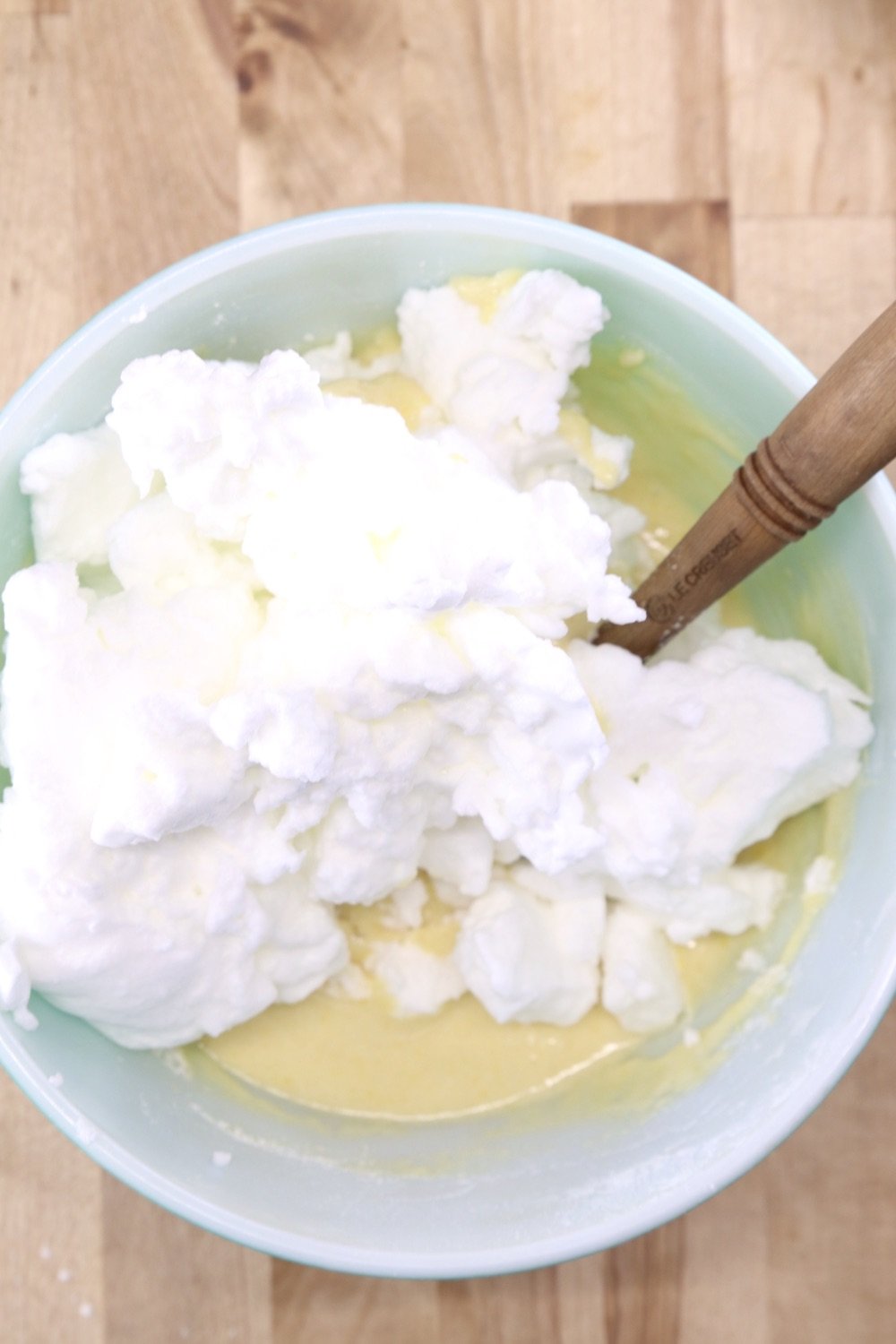 egg whites added to cake batter in a bowl with spatula