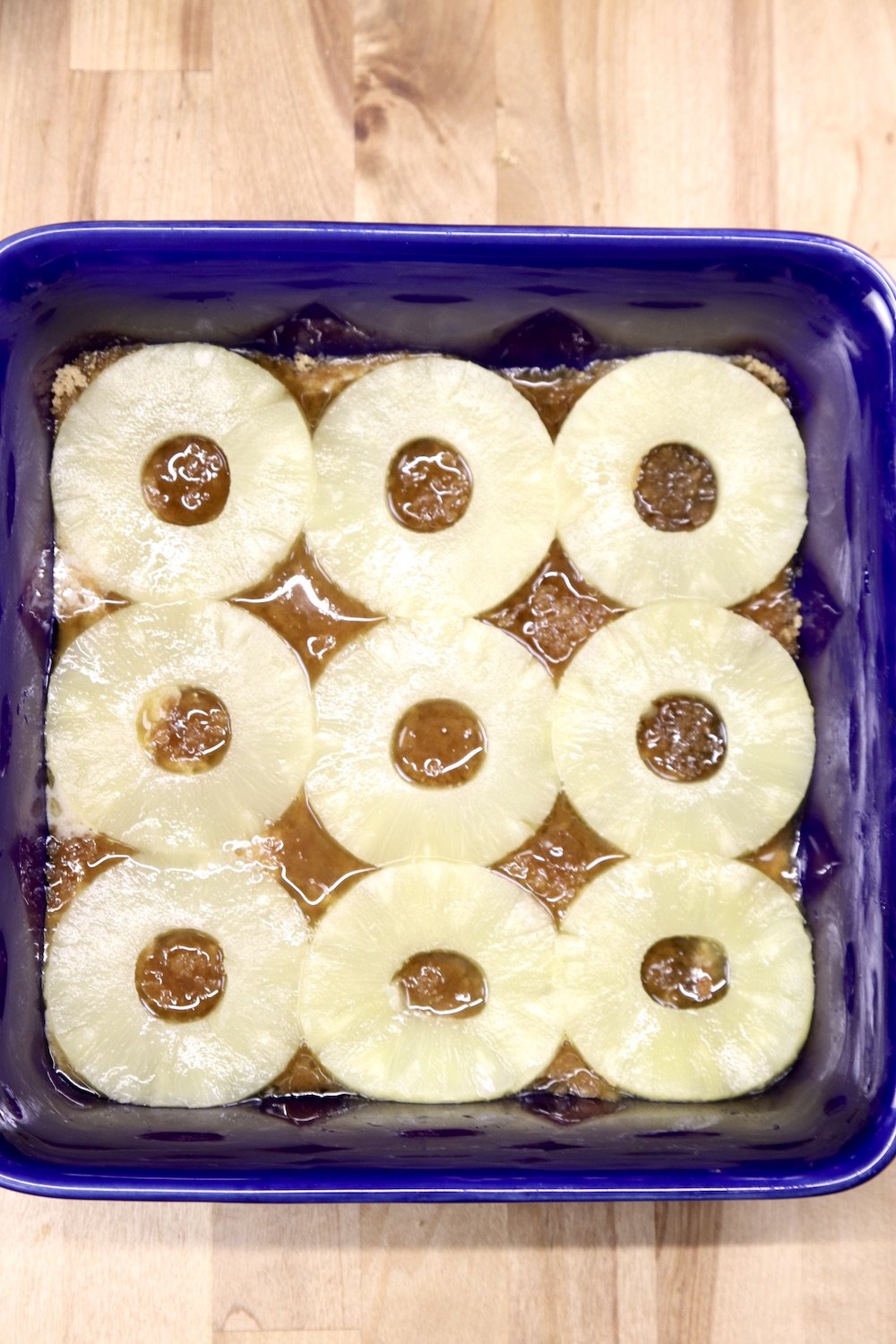 9 pineapple rings over brown sugar mixture in a blue baking dish