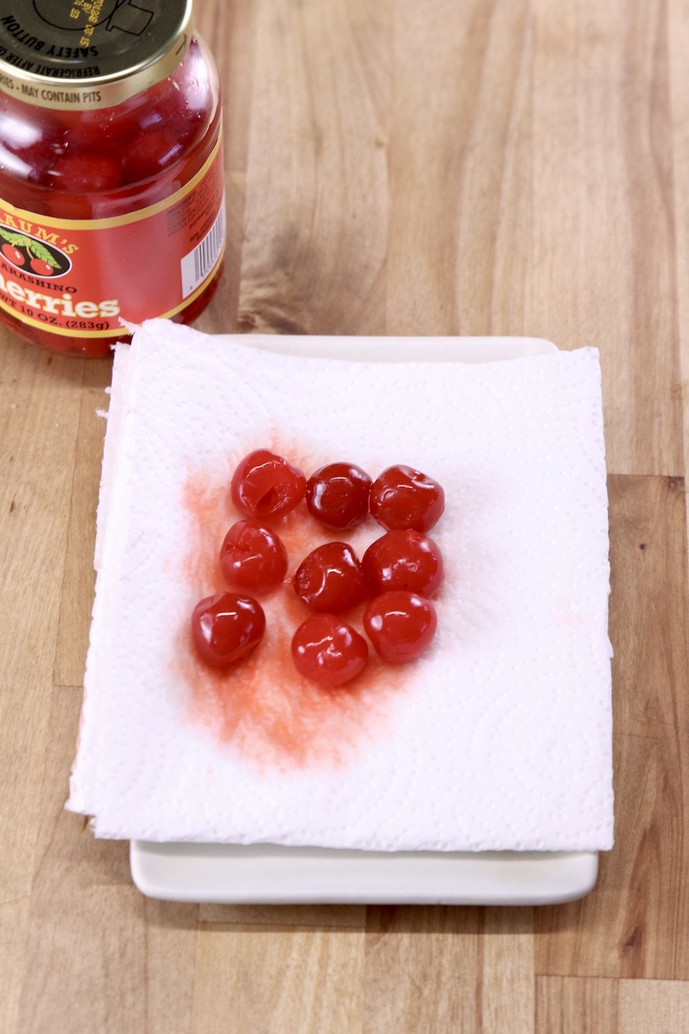 maraschino cherries draining on a paper towel with jar of cherries to the side