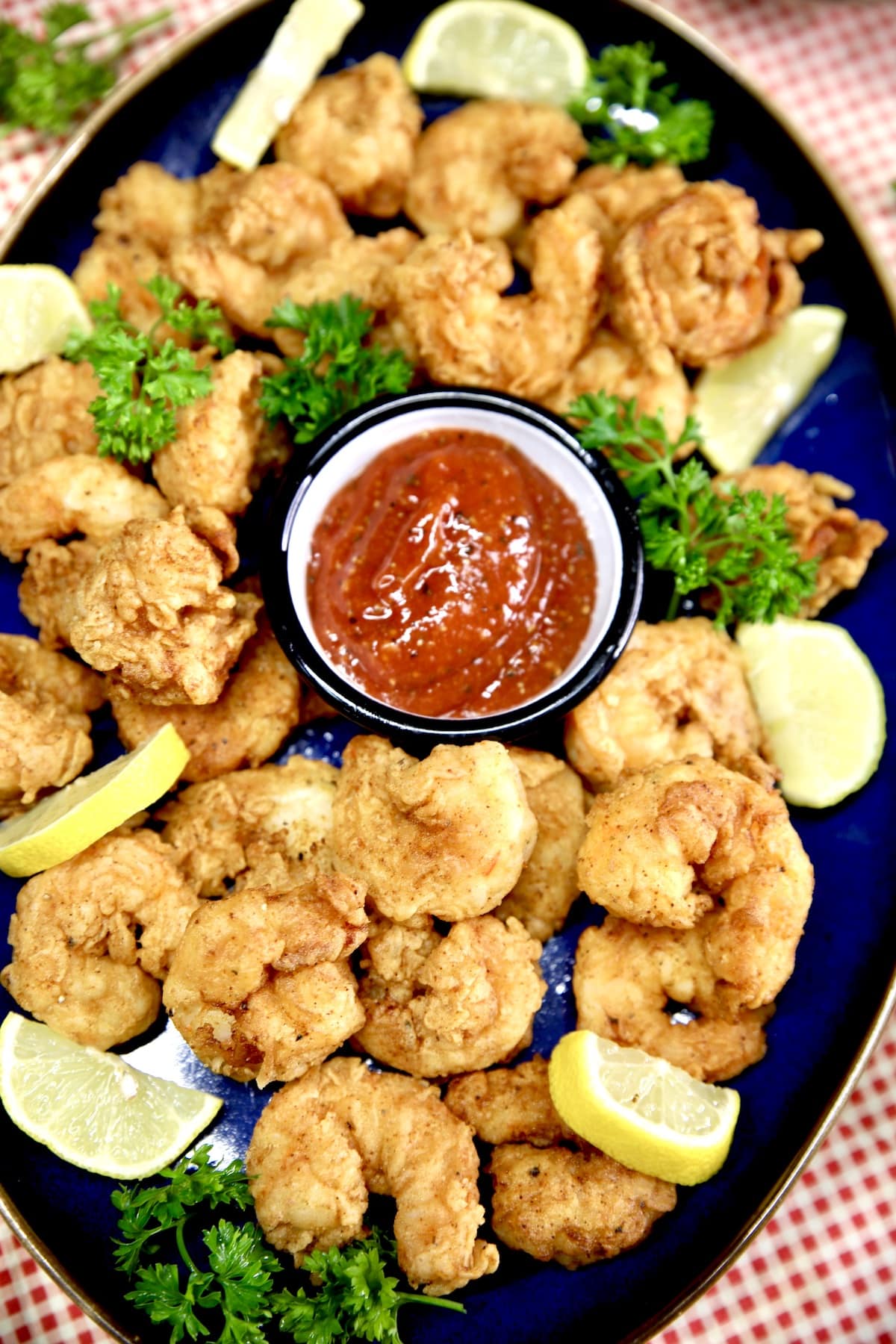 Platter of fried shrimp with cocktail sauce and lemons.