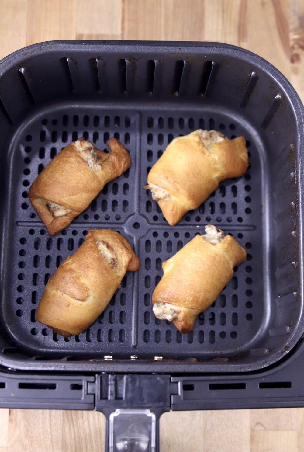 4 cooked sausage cream cheese crescents in air fryer basket