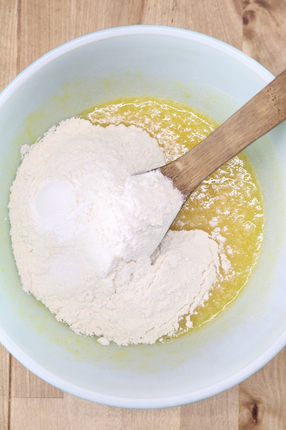 flour added into mixing bowl with eggs and sugar, wooden spoon
