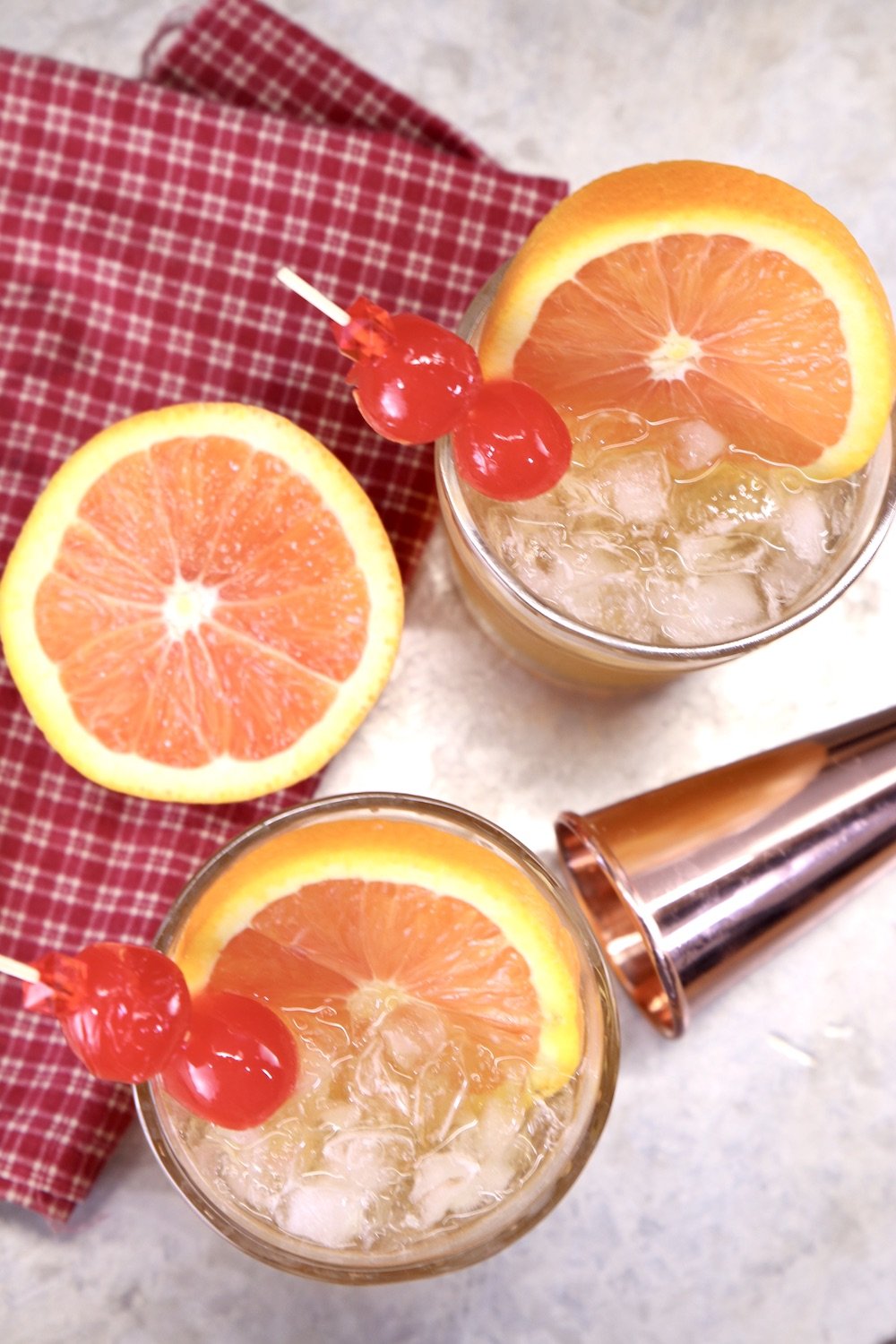 Amaretto Sour Cocktails - garnished with orange slices and cherries, cocktail jigger and half an orange on the tray