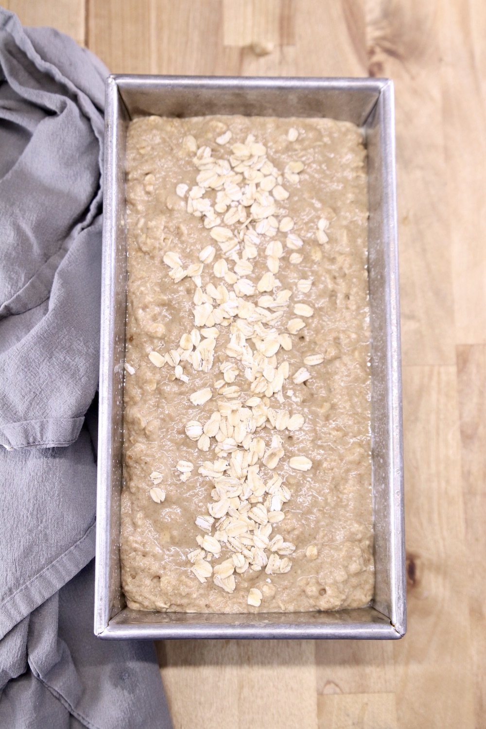 loaf pan with brown bread batter topped with a few oats