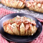 Shallow black bowl with a hasselback potato topped with pizza sauce and cheese