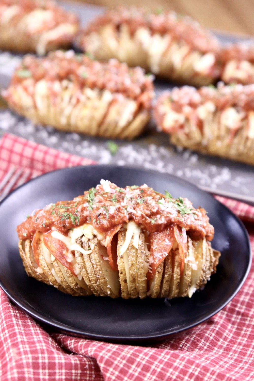 pepperoni pizza topped hasselback potato plated and platter of potatoes in back ground
