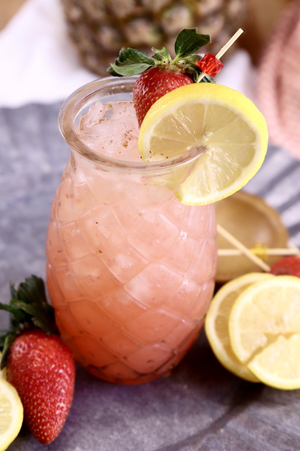 Pineapple shaped glass with pink cocktail, lemon slice and fresh strawberry garnish